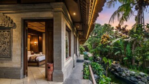 A traditional building with a bed, a stone wall, and a garden with a water feature. - Villa Sujati (Ubud)
