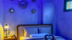 Un dormitorio con cama, almohadas, mesita de noche con lámpara y adornos en la pared.