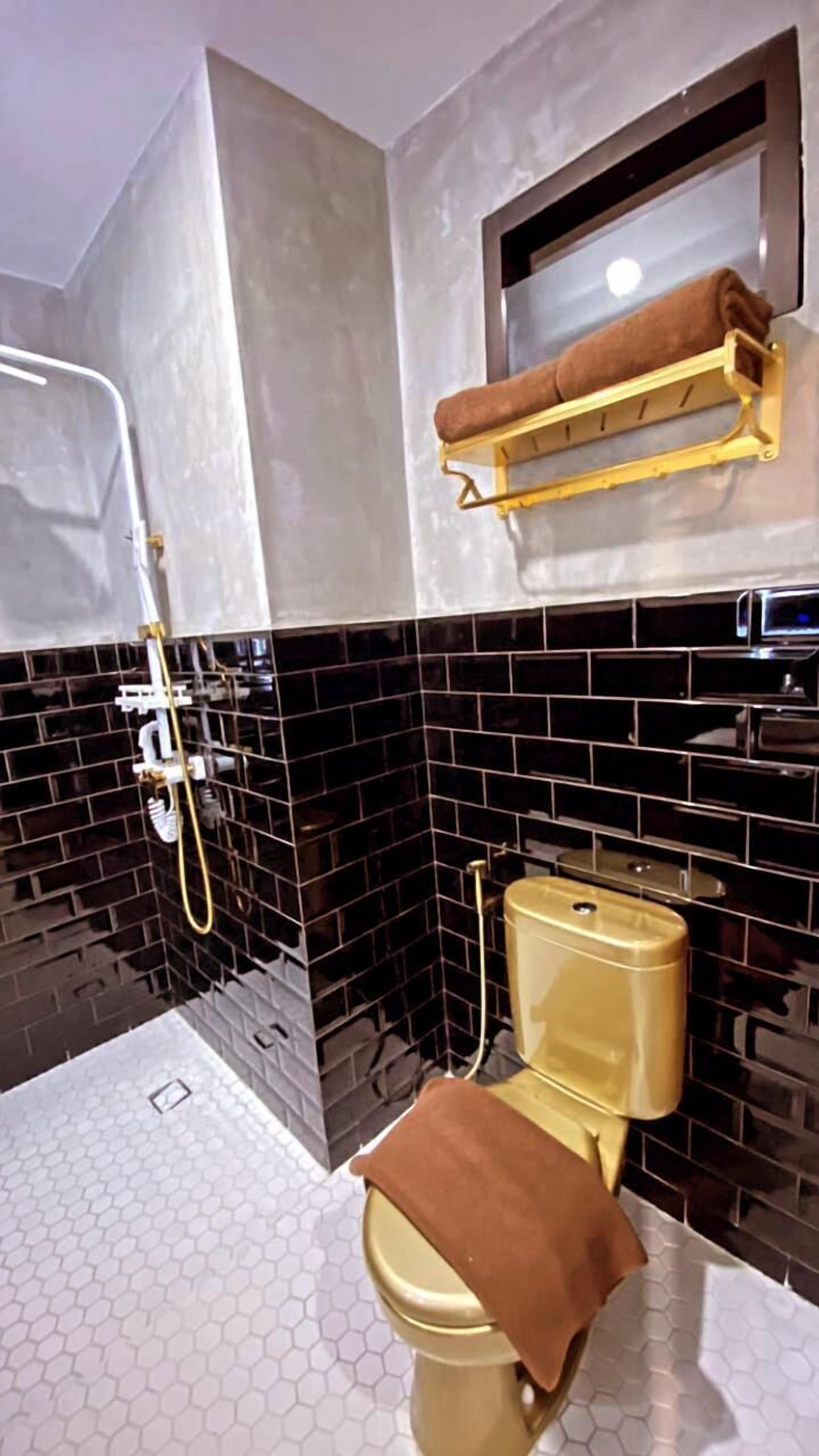 Une salle de bain avec un mur recouvert de carreaux noirs et blancs, des toilettes dorées et un porte-serviettes sur lequel est posée une serviette marron.