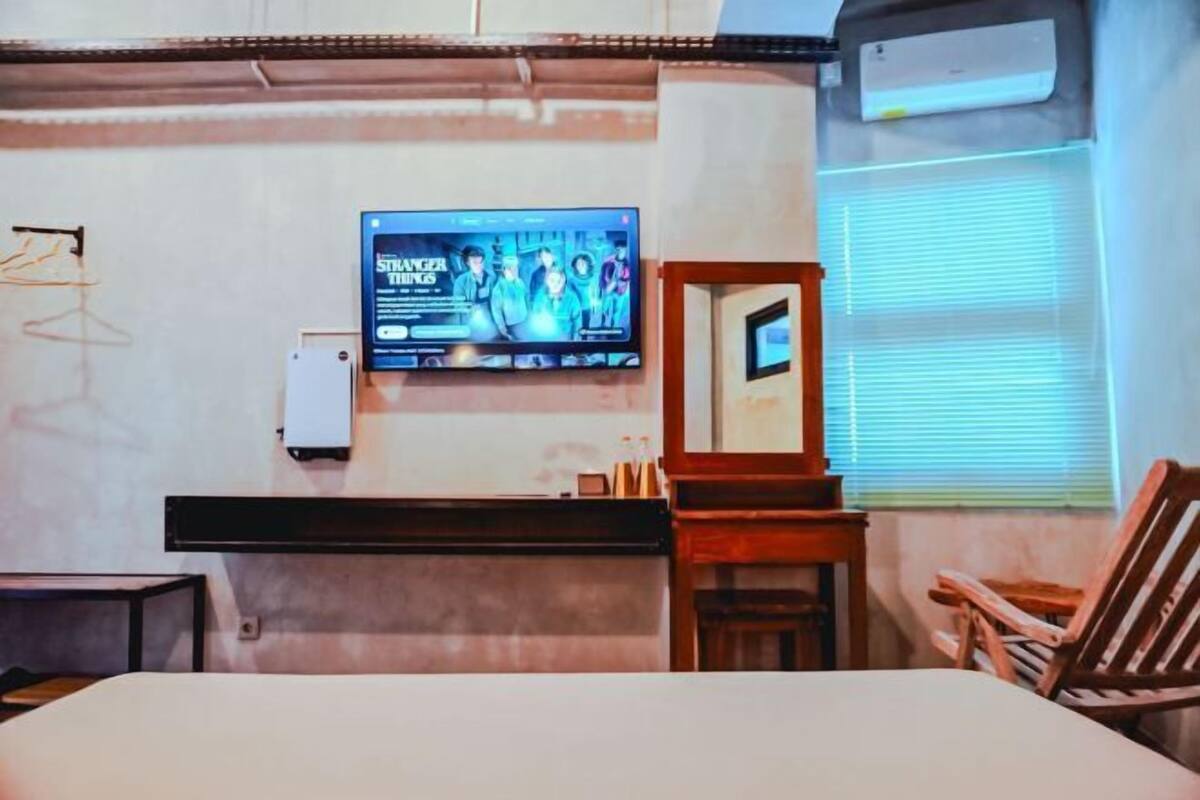 A hotel room with a bed, a TV mounted on the wall, a wooden chair, and a window with blinds.