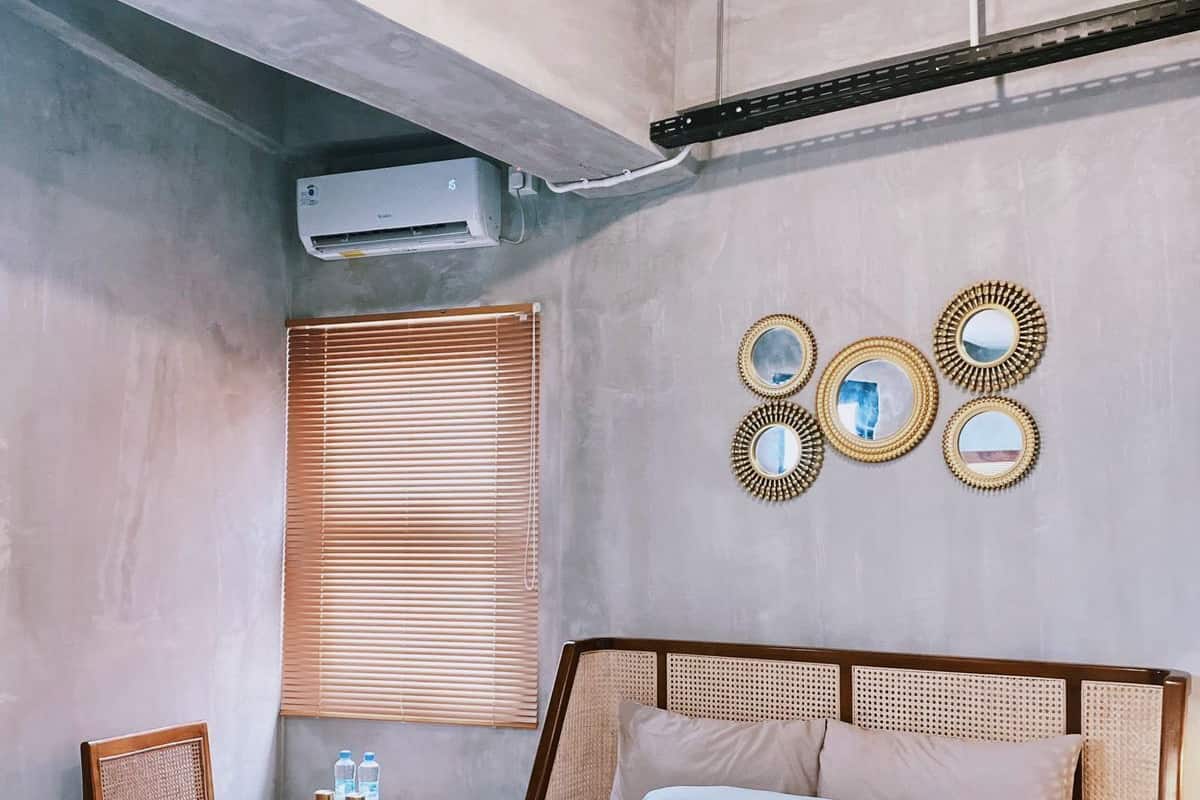 Un dormitorio con cama, una silla, una mesita y un equipo de aire acondicionado, además de espejos decorativos en la pared.