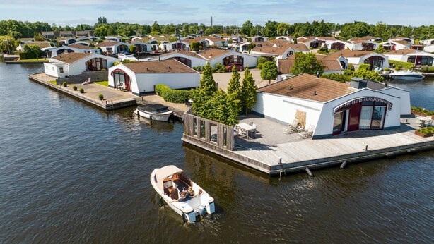 En småbåtshamn med flera mindre båtar förtöjda, omgiven av moderna, kompakta hus med platta tak och stora fönster.
