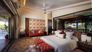 Une chambre moderne avec un grand lit, un canapé rouge, un plancher en bois et une grande fenêtre donnant sur des palmiers.