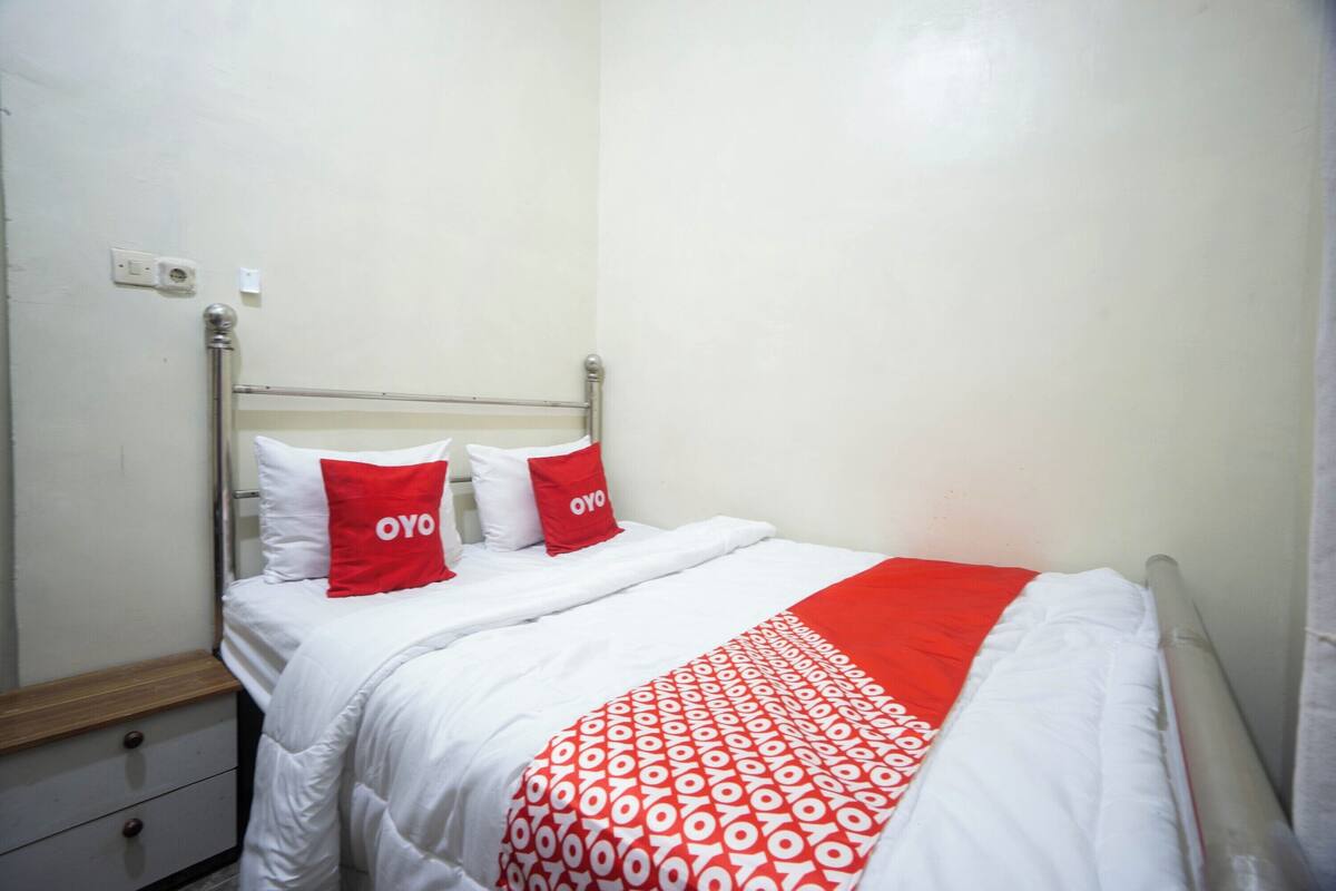 A hotel room with a bed, two pillows, a bedside table, and a nightstand.