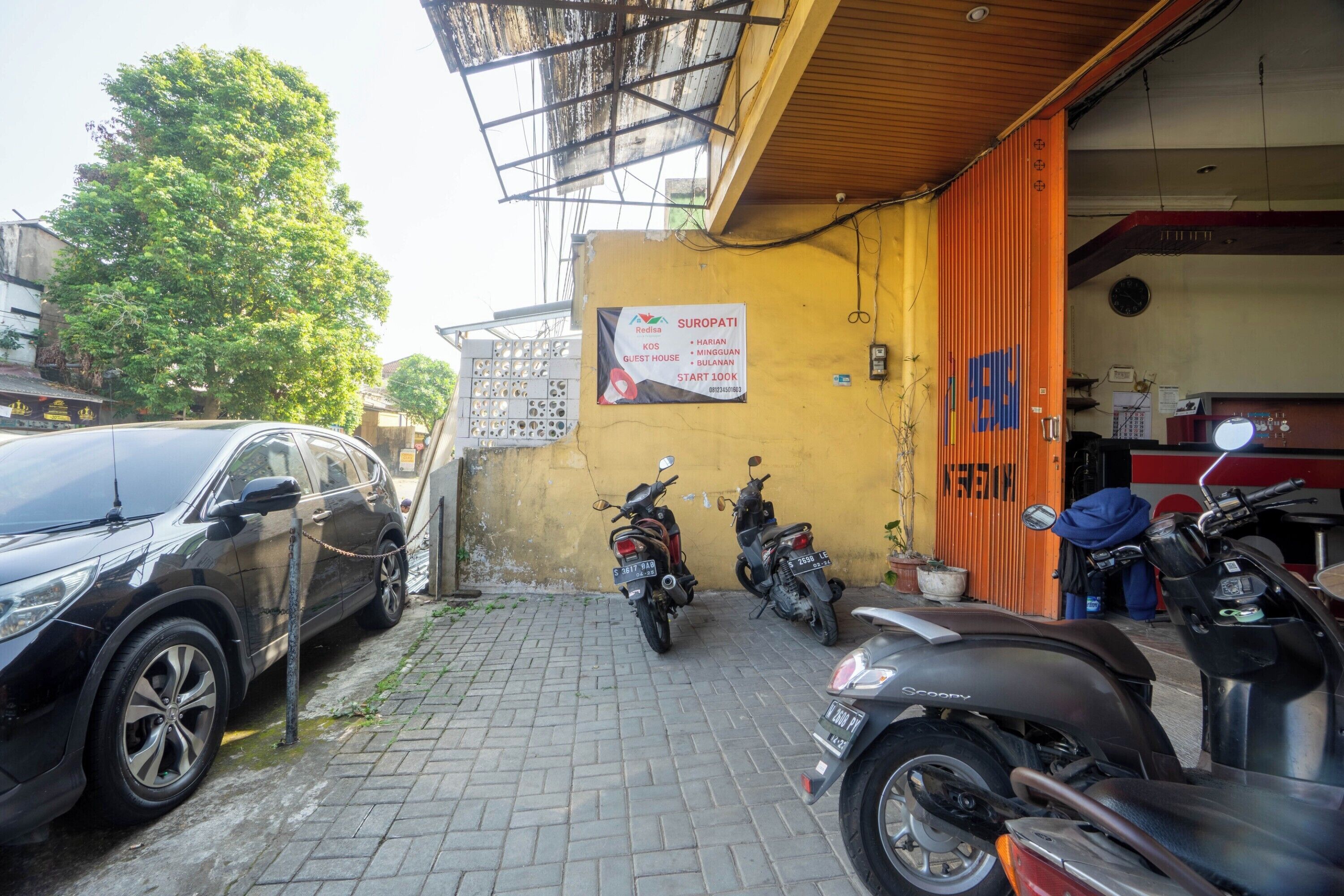 A parking area with a black SUV and several motorcycles parked. There is a sign on the wall advertising a guest house.