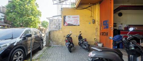 A parking area with a black SUV and several motorcycles parked. There is a sign on the wall advertising a guest house.