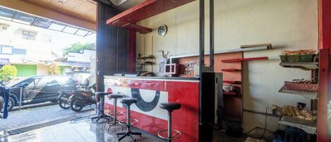 A restaurant with a red counter, stools, a clock, and a refrigerator.