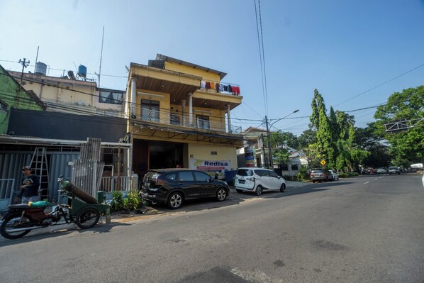 A street view with a two-story building, a parked motorcycle, and several cars. - OYO 93987 Suropati 2 Guest House (Malang)