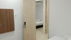 A minimalist hotel room with a wooden wardrobe, a bed with white bedding, and a visible air conditioning unit. - GoHome Harmoni Apartment (Jakarta)