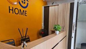 A reception desk with a 'HOME' sign, a potted plant, and a fan. - GoHome Harmoni Apartment (Jakarta)