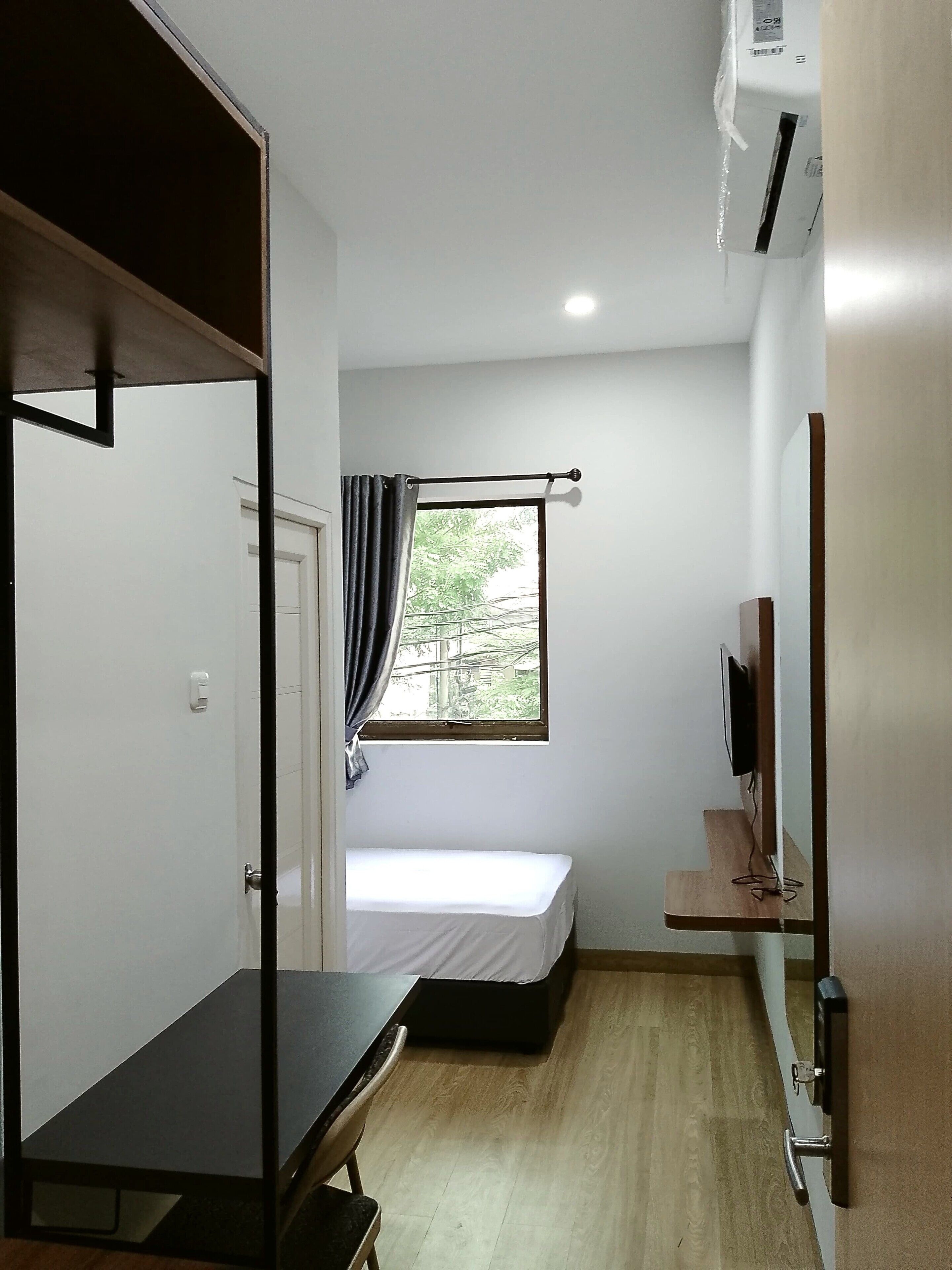 Una habitación pequeña con cama, escritorio, televisor y ventana con cortinas.