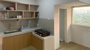 A compact kitchen with wooden cabinets, a sink, and a gas stove. There is a window providing a view of the outside. - GoHome Harmoni Apartment (Jakarta)