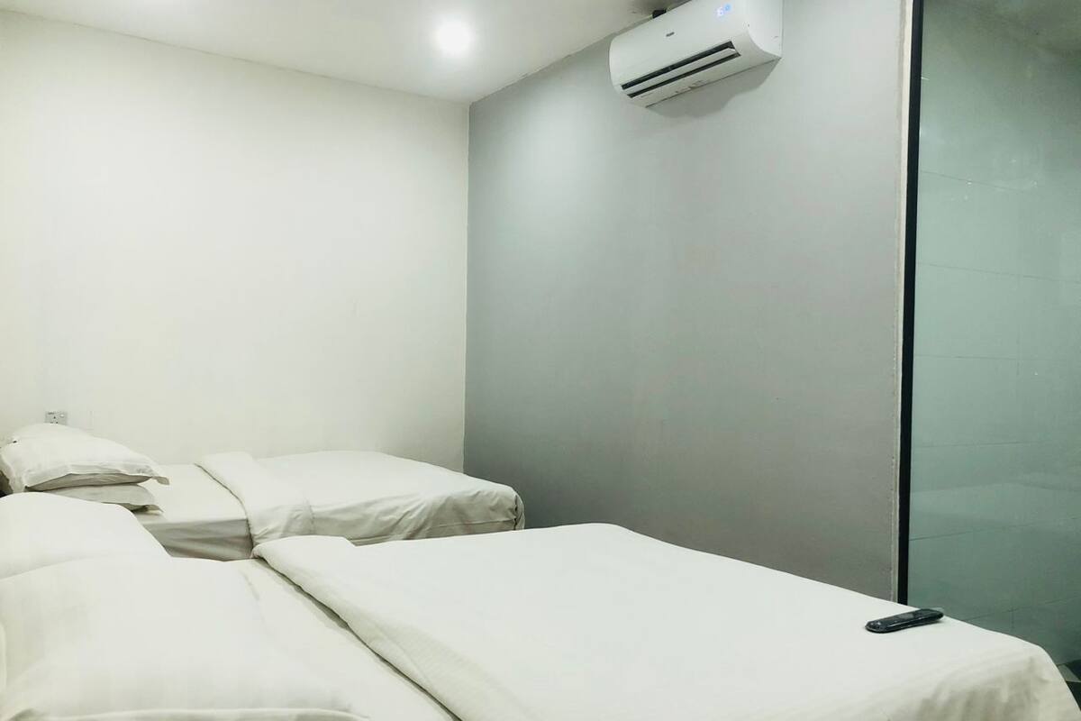 Une chambre avec deux lits simples, un climatiseur fixé au mur et une cloison en verre.