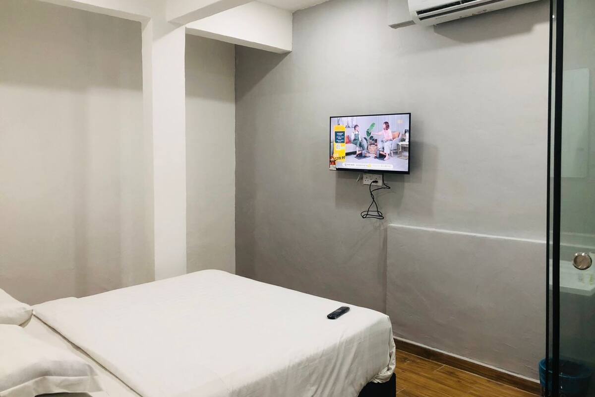 Une chambre d’hôtel avec un lit simple, un téléviseur fixé au mur et un appareil de climatisation.