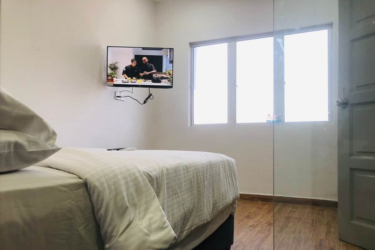 Une chambre à coucher avec un lit, un téléviseur fixé au mur, une fenêtre et une porte.