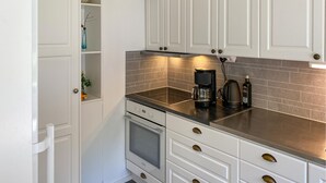 Une cuisine moderne avec des meubles blancs, un plan de travail en acier inoxydable, un four encastré et une machine à café.