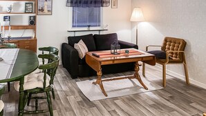 Un salon avec une table basse en bois, un canapé noir, un fauteuil vert, un fauteuil à rayures et une lampe.