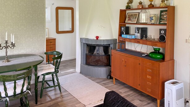 Een kamer met een eettafel, stoelen, een openhaard, een houten kast met diverse spullen, en een radiator.