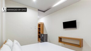Een slaapkamer met een bed, een aan de muur bevestigde televisie en een klein houten plankje.