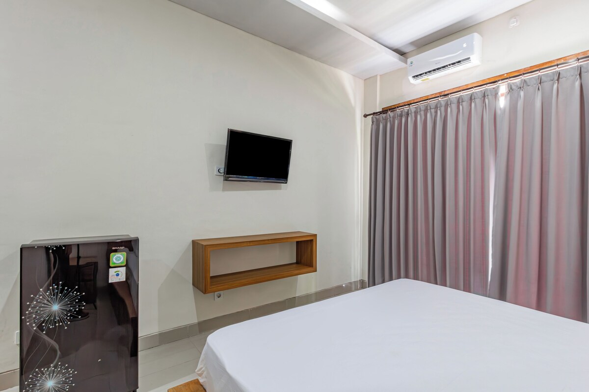 A hotel room with a bed, a TV mounted on the wall, a wooden shelf, and a curtain.