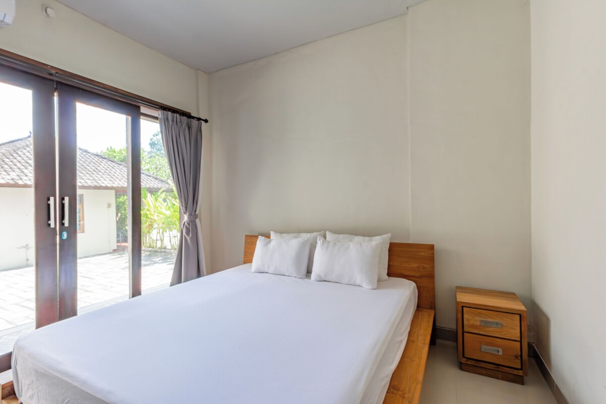 Ein Hotelzimmer mit einem großen Bett, einem Nachttisch aus Holz und einer Schiebeglastür, die zu einem Außenbereich führt.