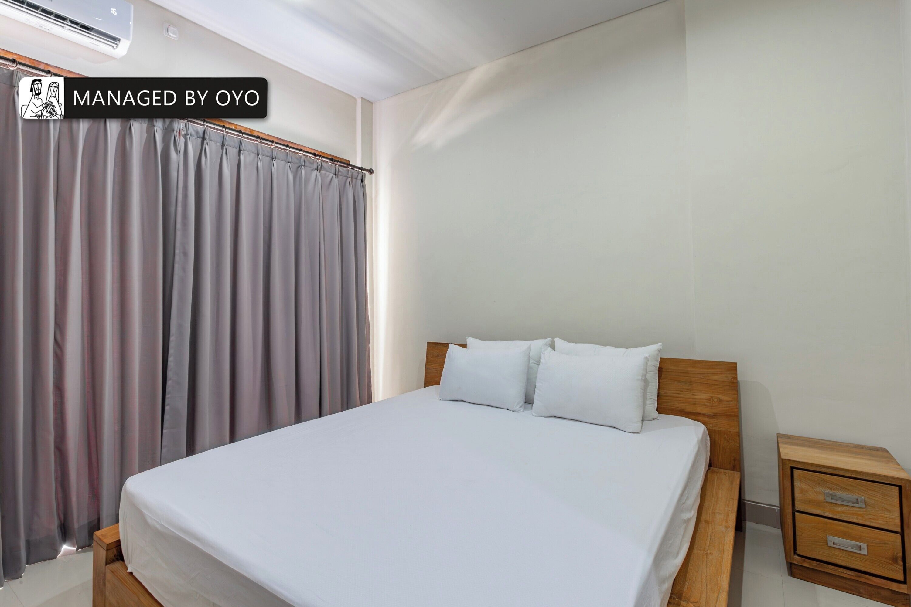 Une chambre à coucher avec un lit, une table de chevet en bois dotée de tiroirs et un rideau gris.