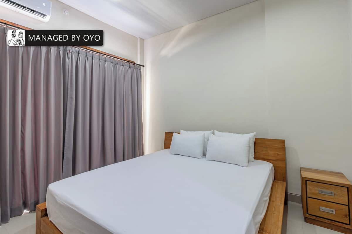 A bedroom with a bed, a wooden nightstand with drawers, and a grey curtain.