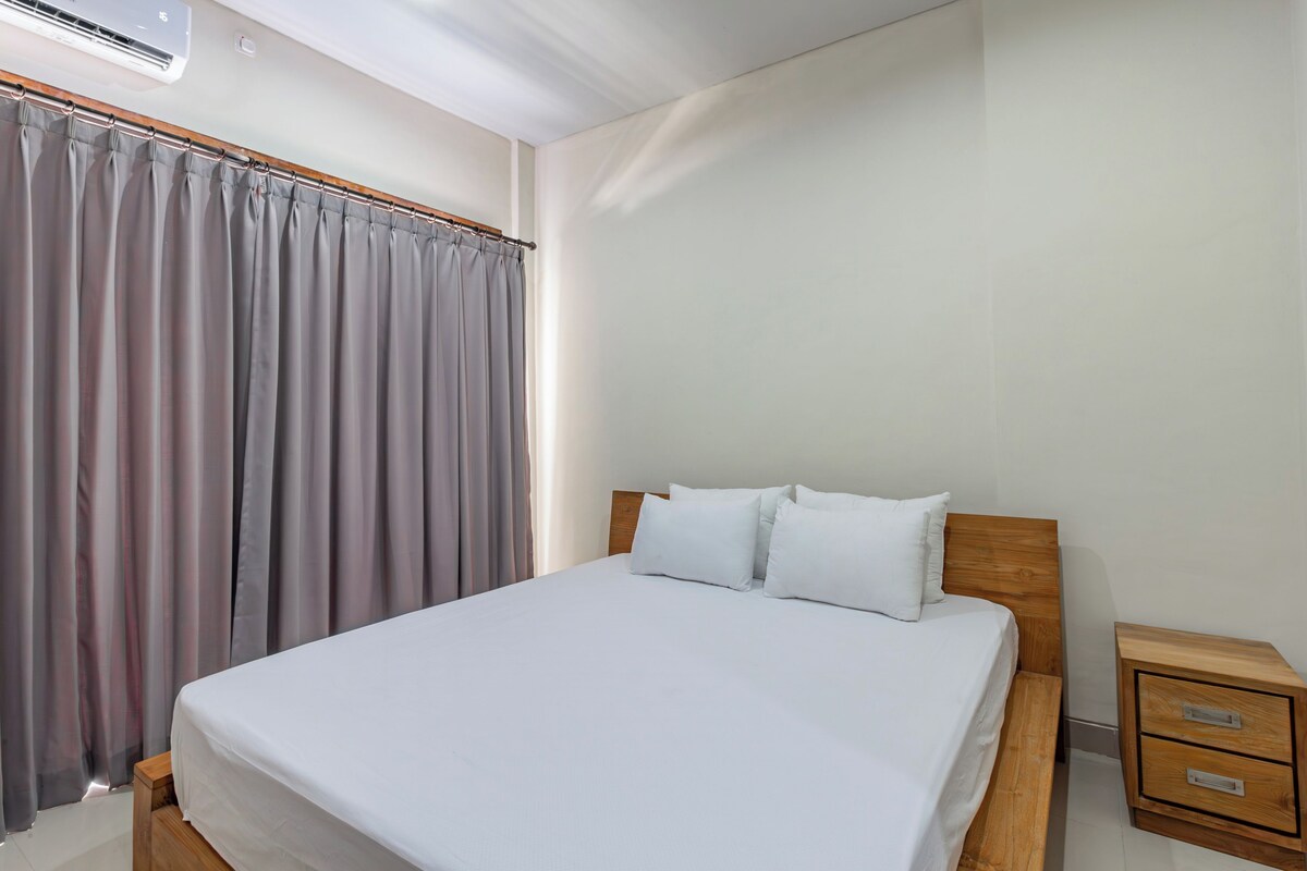 A neatly made bed with white linens, a wooden headboard, and a nightstand with drawers.