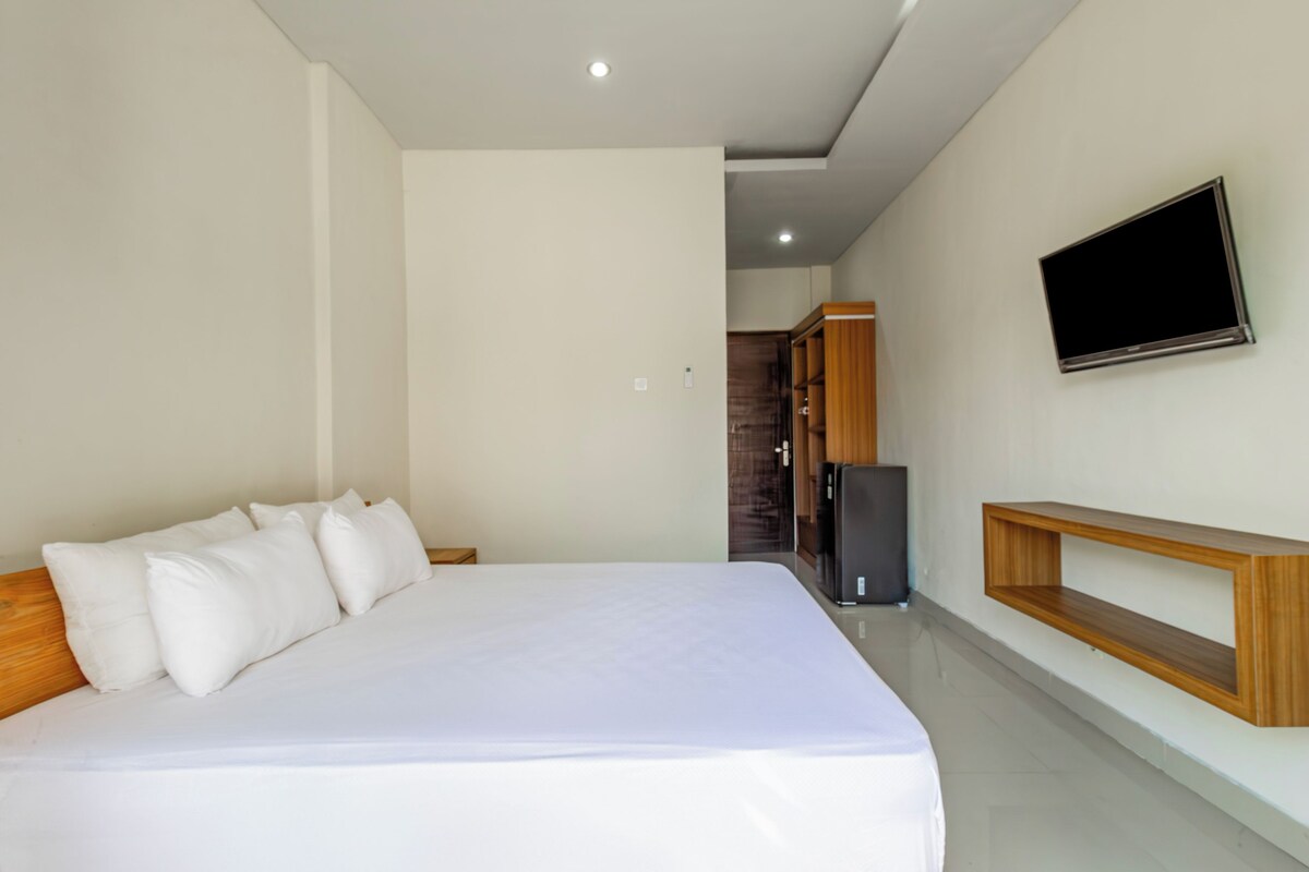 A modern bedroom with a large bed, a TV mounted on the wall, and a built-in wooden shelf.