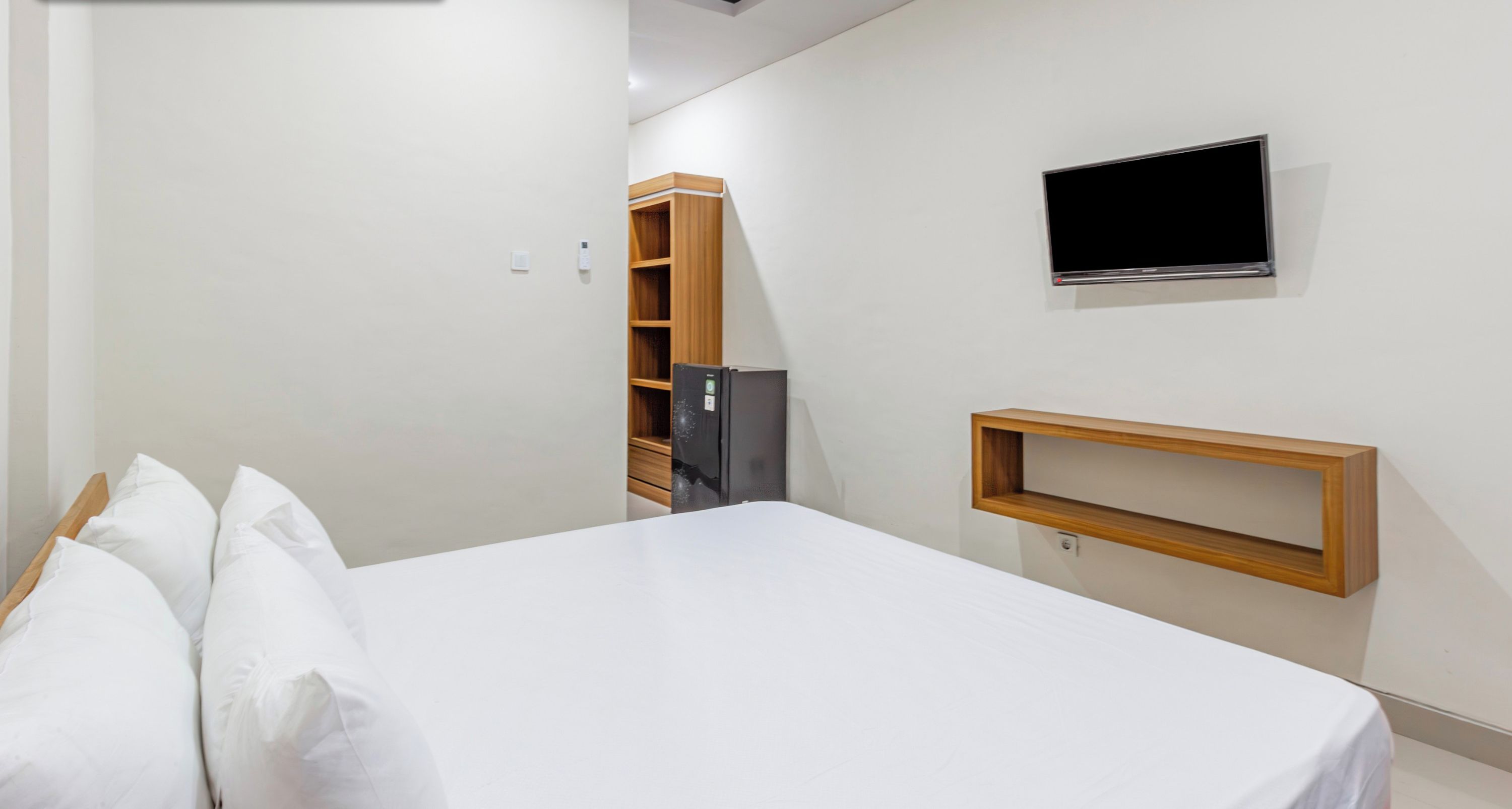 A bedroom with a bed, a television mounted on the wall, and a small wooden shelf.
