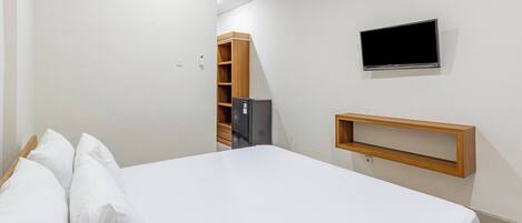A bedroom with a bed, a television mounted on the wall, and a small wooden shelf.