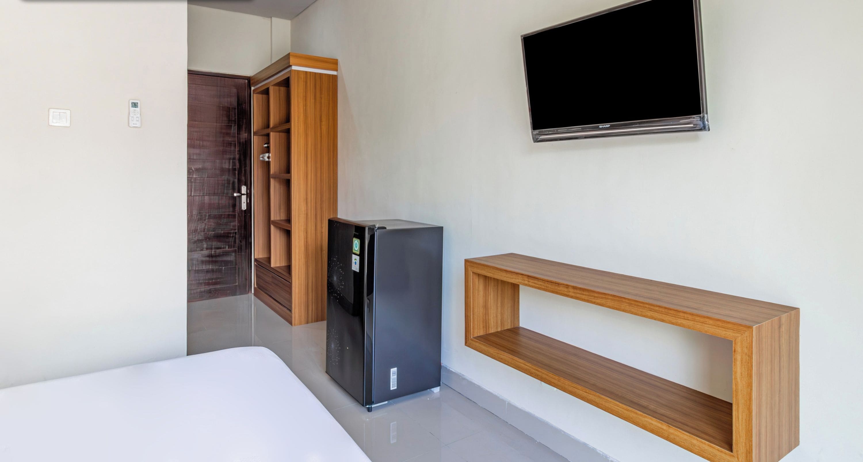 A modern room with a flat-screen TV mounted on the wall, a black refrigerator, a wooden shelf, and a wardrobe with a mirror.