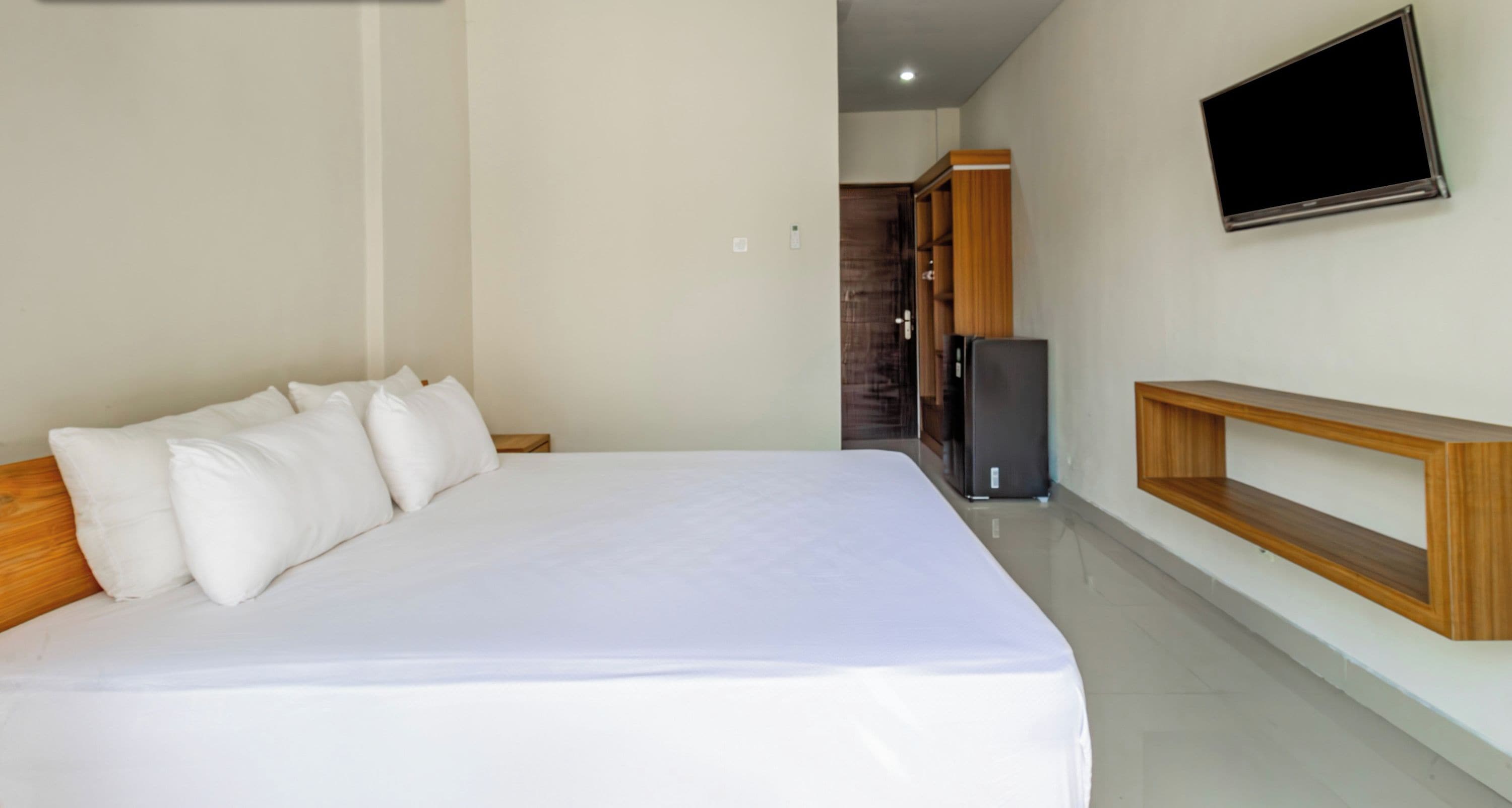 A modern hotel room with a large bed, a flat-screen TV mounted on the wall, and a wooden console table.