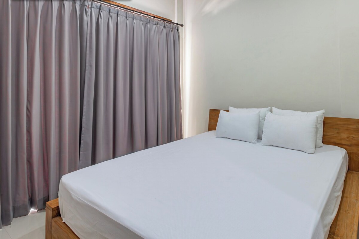 A bedroom with a bed, a wooden nightstand with drawers, and a grey curtain.