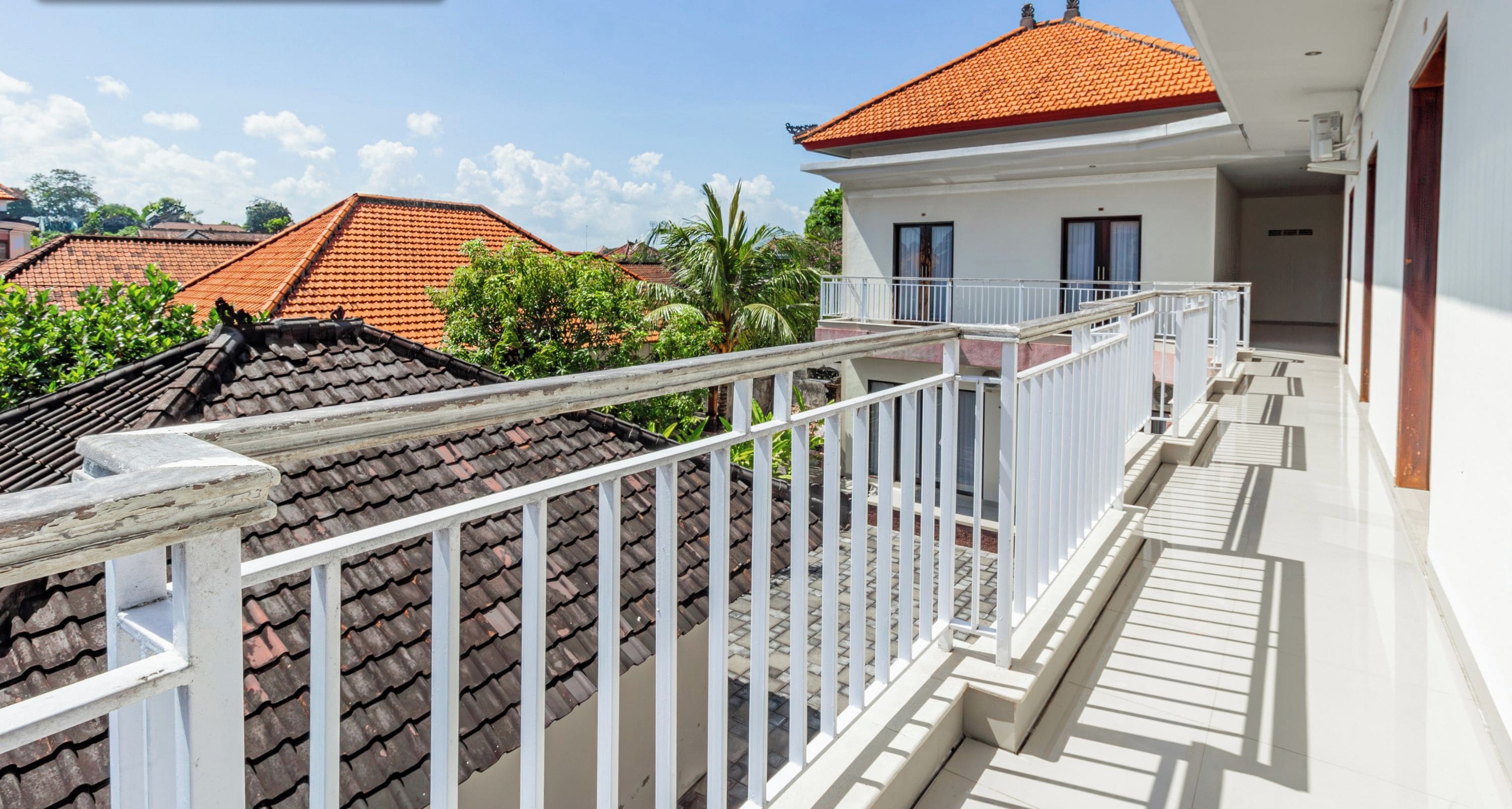 A residential building with a red-tiled roof, white exterior walls, and a balcony with white railings.