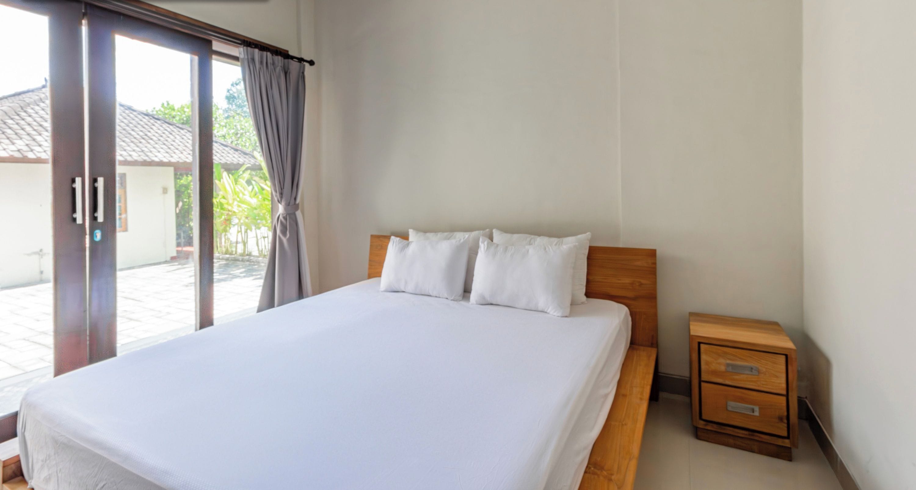 A bedroom with a large bed, a wooden nightstand, and a sliding glass door leading to an outdoor area.