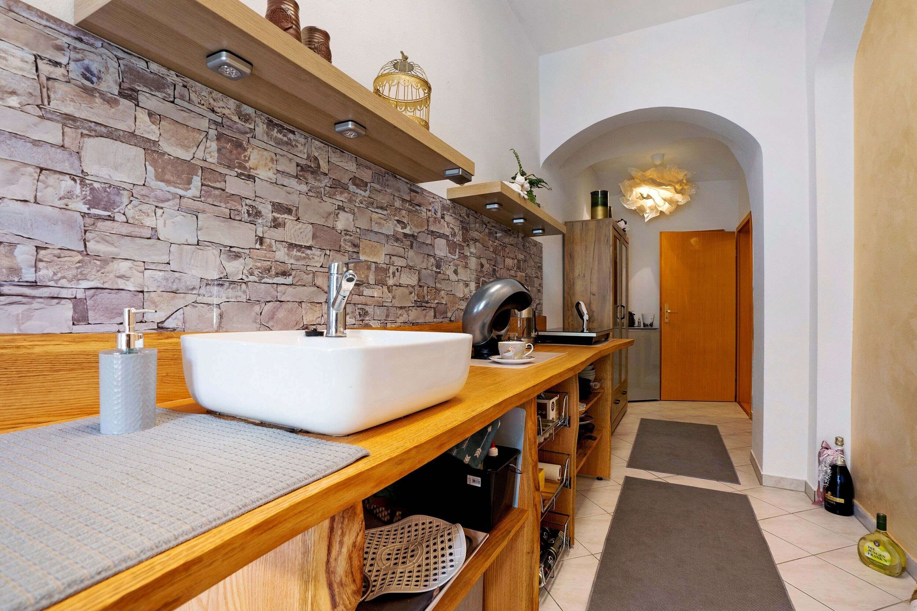 A modern bathroom with a stone wall, wooden vanity, and a large sink.