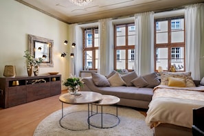 Une chambre meublée comprenant un canapé, un lit, une table basse ronde, un meuble et de grandes fenêtres avec des rideaux.