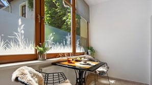 A room with a dining table, chairs, a radiator, and a window with a view of greenery.