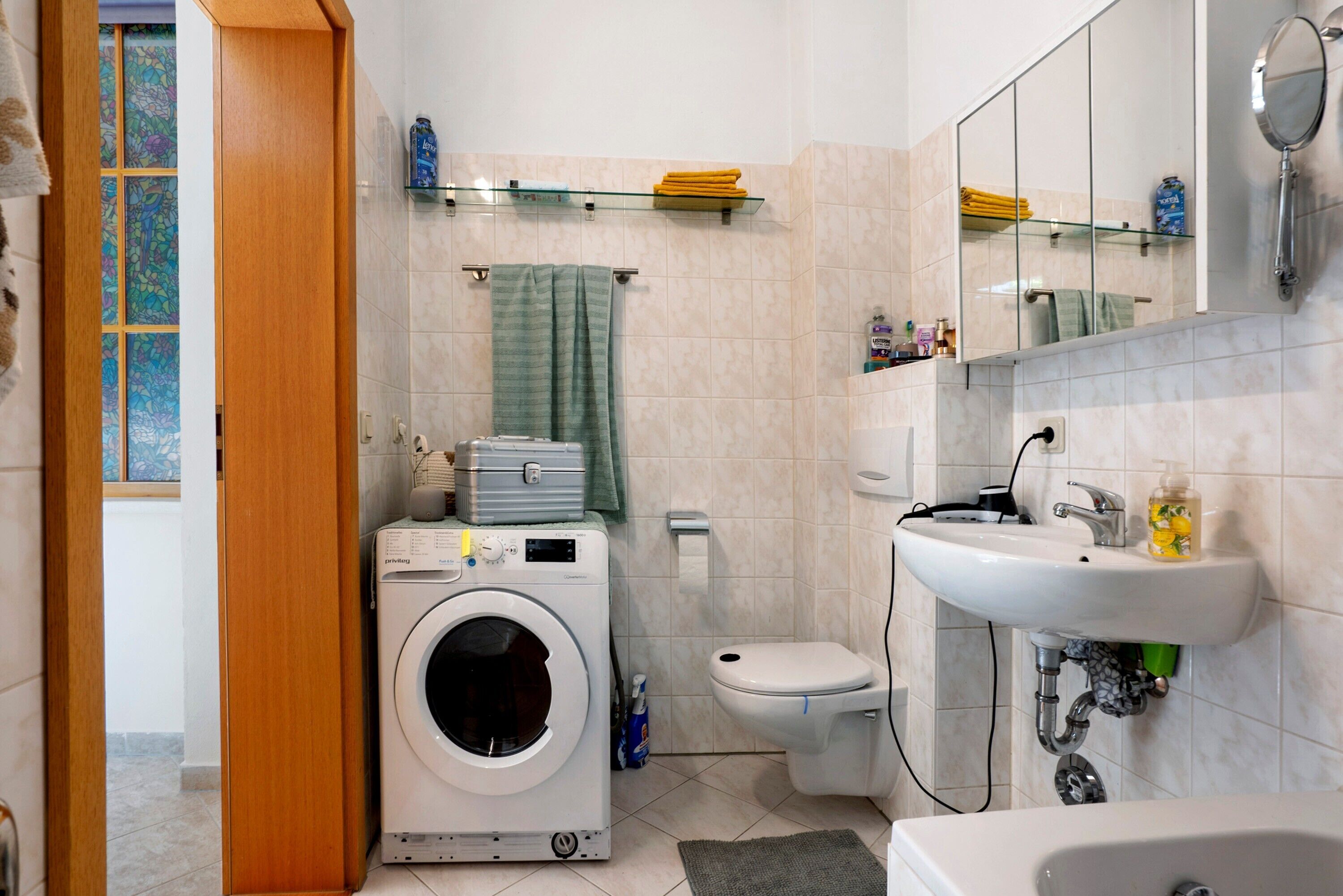 A bathroom with a washing machine, toilet, sink, and a mirror.