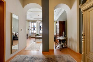A hallway with a mirror, a wooden floor, a rug, a cabinet, and a shelf with bottles.