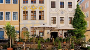 A building with multiple windows, outdoor seating with umbrellas, and potted plants.