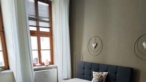 A bedroom with a bed, a chair, a radiator, and a window with curtains.