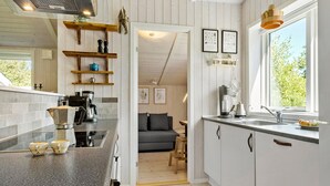 Cocina moderna con horno empotrado, cafetera y lavabo. Se aprecia una ventana con vistas a la vegetación.