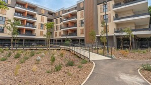 A multi-story residential building with balconies, a central courtyard with pathways, and a parking area.