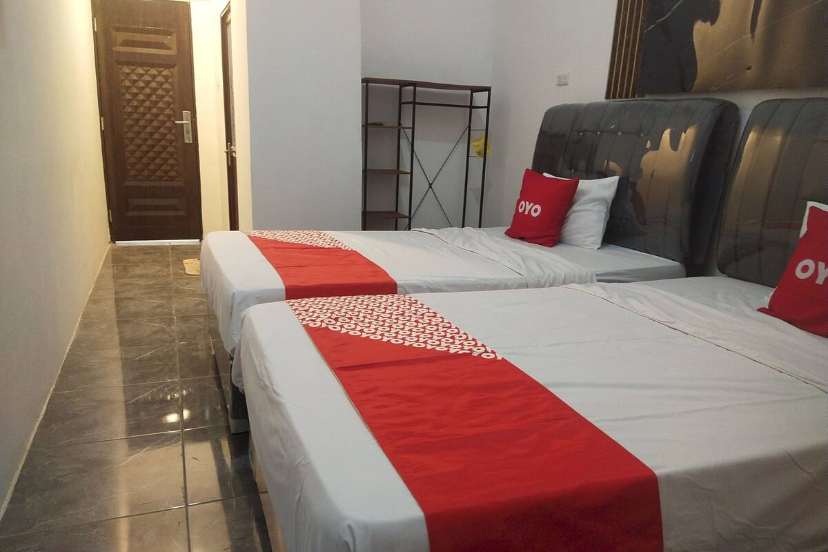 Habitación de hotel con dos camas, cada una con colcha roja y blanca y un cojín con la palabra "OYO".
