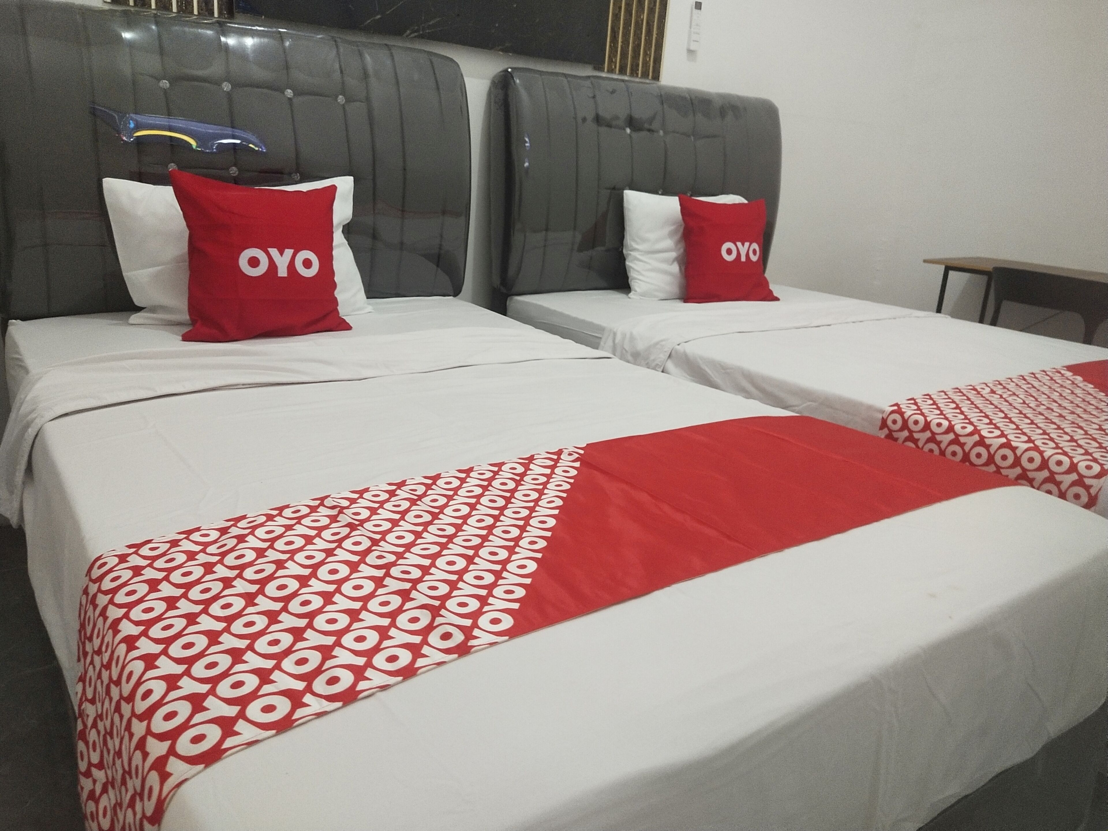 Two beds with grey headboards, white bedding, and red pillows with "OYO" branding.