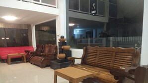 Ein geräumiger Wohnbereich mit hoher Decke, einem roten Sofa, Holzsesseln, einem Couchtisch und einem großen Fenster mit Blick auf die Stadt.