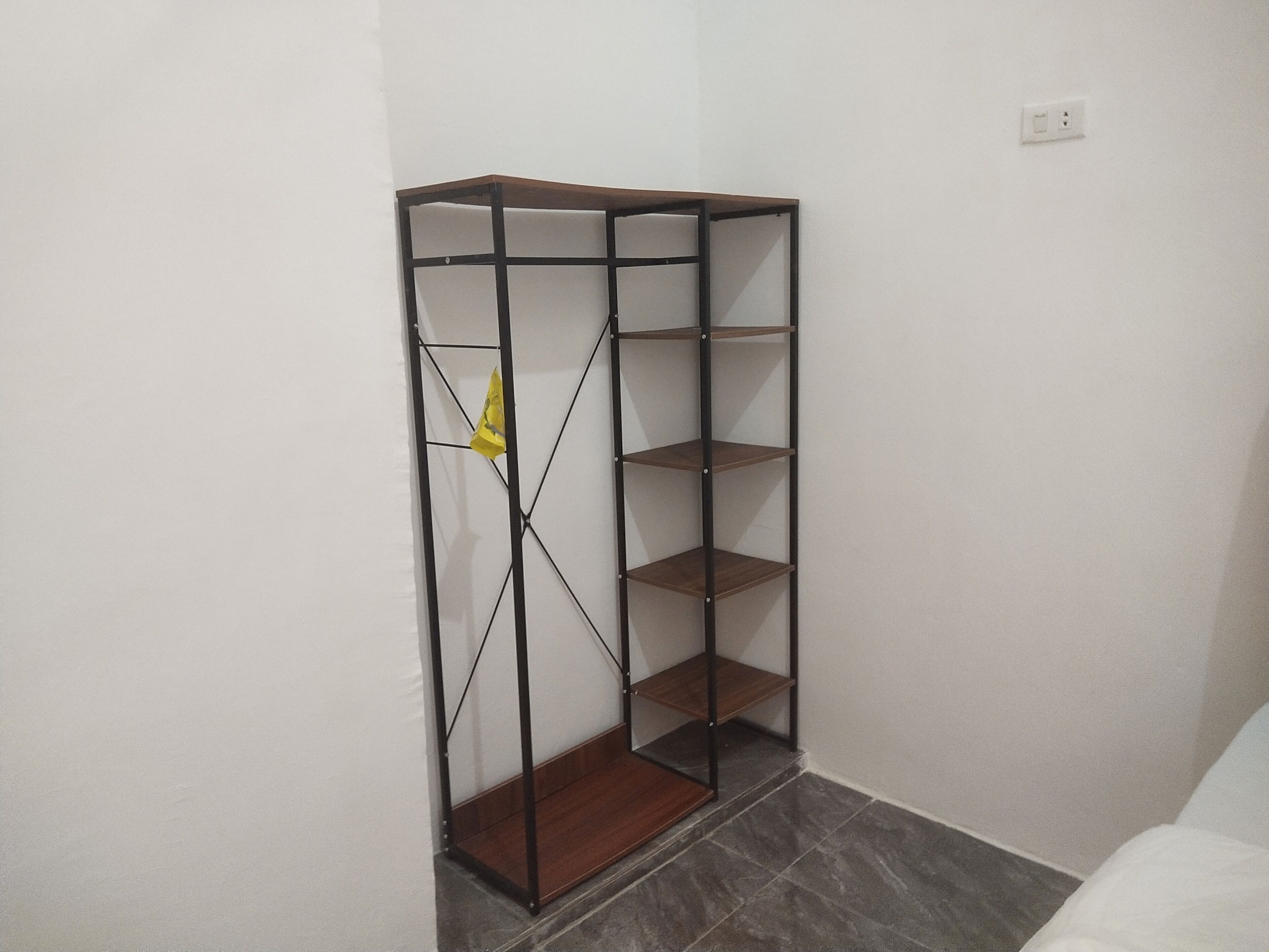 Eine Eckgarderobe mit offenen Regalen und einer Holzboden, vor einer schlichten Wand.