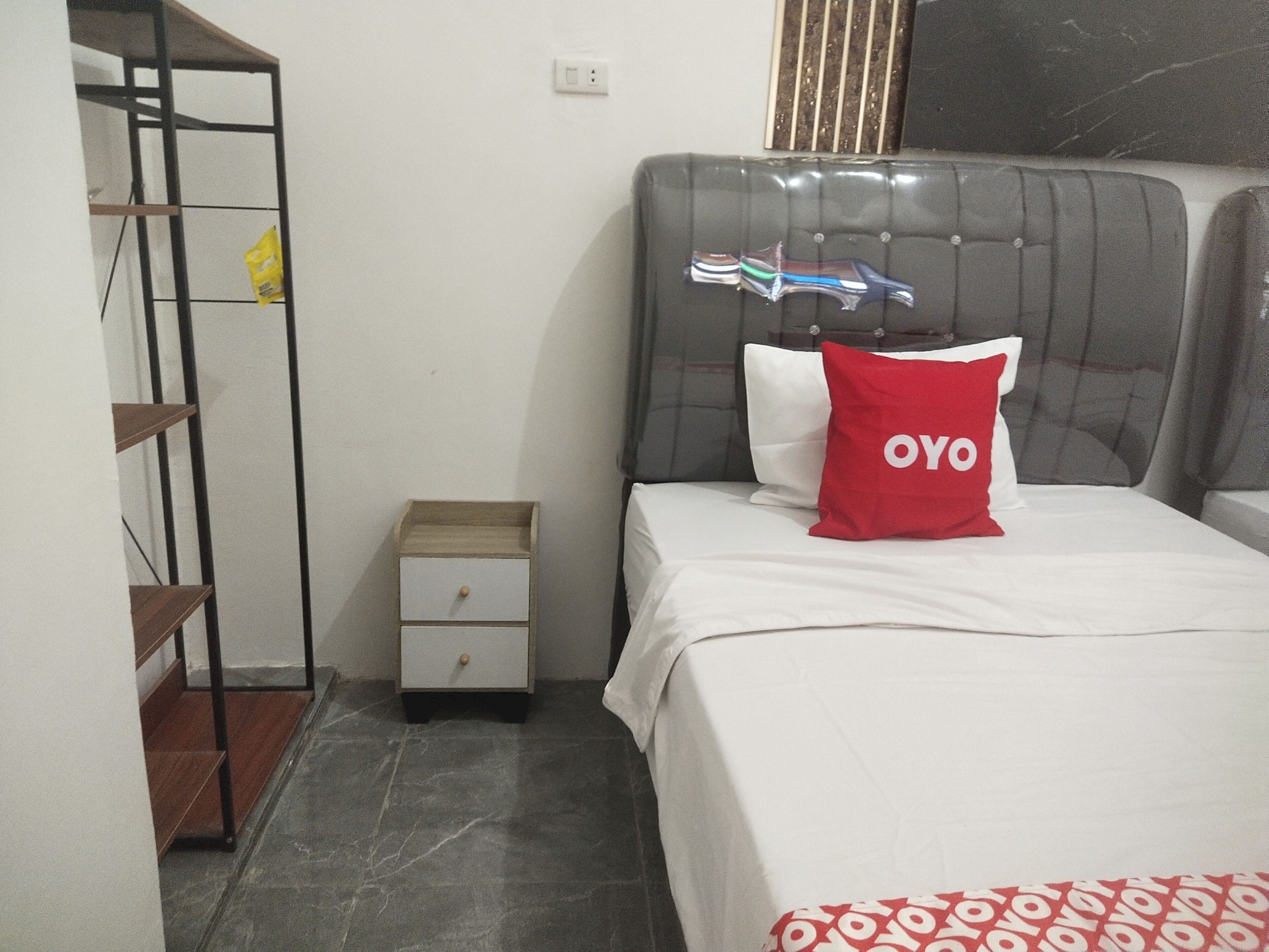 A bedroom with a bed, a nightstand, a wooden shelf unit, and a window with blinds.